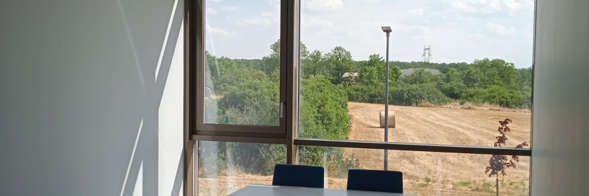 Salle de réunion avec table, chaises, poubelle, fenêtres et climatisation.