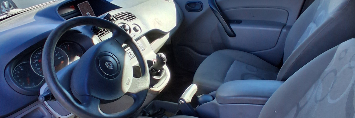 Intérieur de voiture avec volant, siège conducteur et passager, rétroviseur intérieur, pédales et autre voiture en arrière-plan.