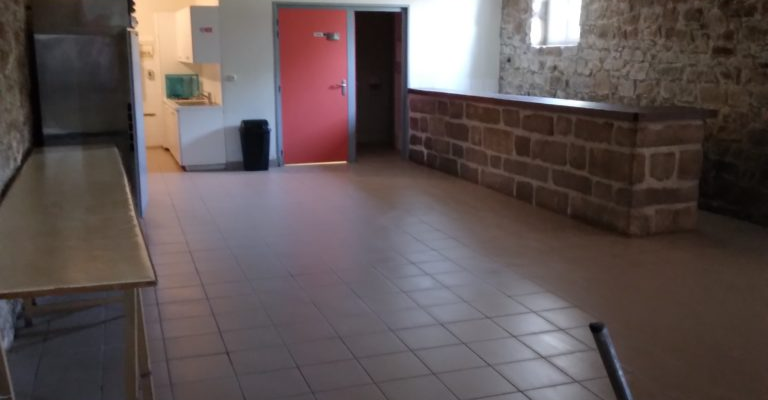 Pièce avec table, porte rouge, lavabo et miroir. Lumière allumée au plafond.