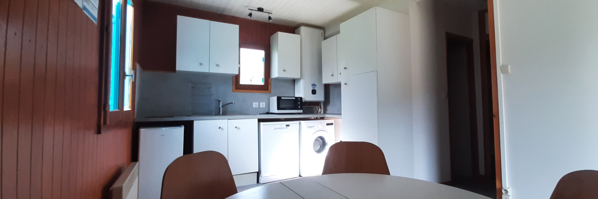 Cuisine avec table, chaises, électroménagers, armoires, et suspension.