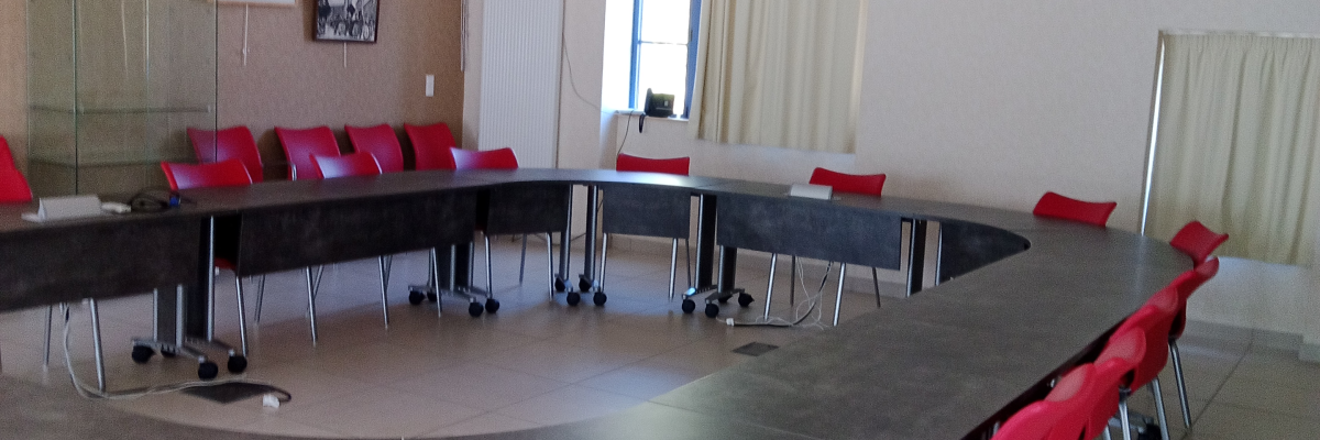 Salle de réunion avec table, chaises, vidéo projecteur, écran et rideaux.