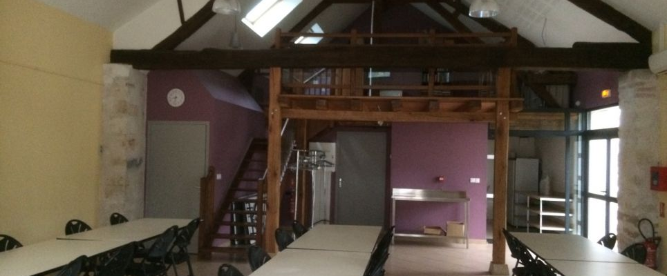 Salle avec tables, chaises, escaliers, et poubelle. Structure en bois.