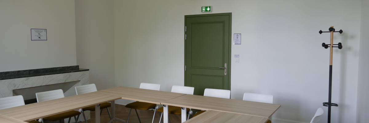 Salle avec table rectangulaire, chaises, porte verte, porte-manteau et climatisation.
