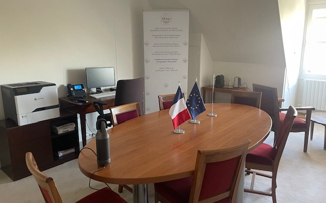 Pièce avec table, chaises, ordinateur, imprimante, et deux drapeaux.
