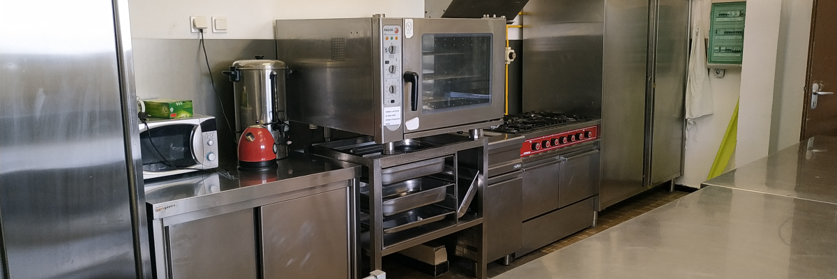 Cuisine professionnelle avec four, cafetière, micro-ondes, friteuse, réfrigérateur et plan de travail.