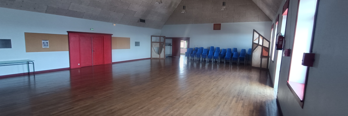 Salle avec parquet, chaises, portes rouges, fenêtres et lumières suspendues.