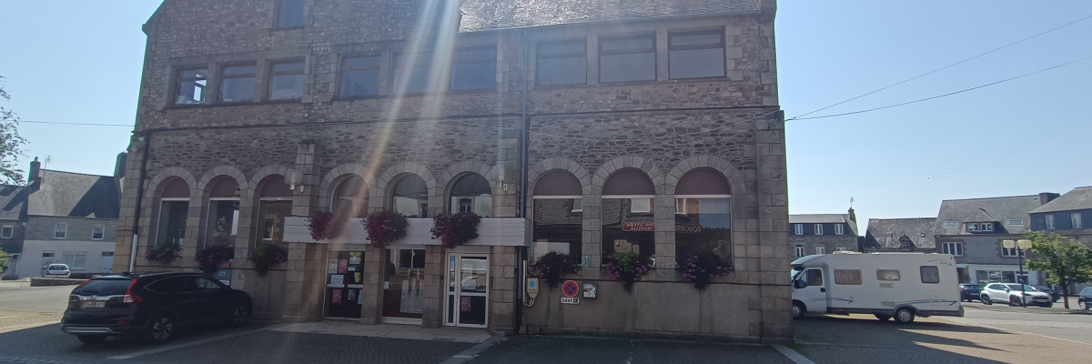 Bâtiment en pierre avec voitures et camping-car garés devant.