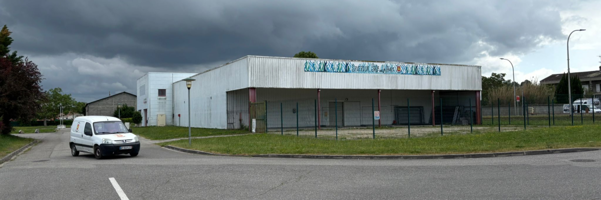 Bâtiment industriel avec enseigne, voiture blanche, route et lampadaires.
