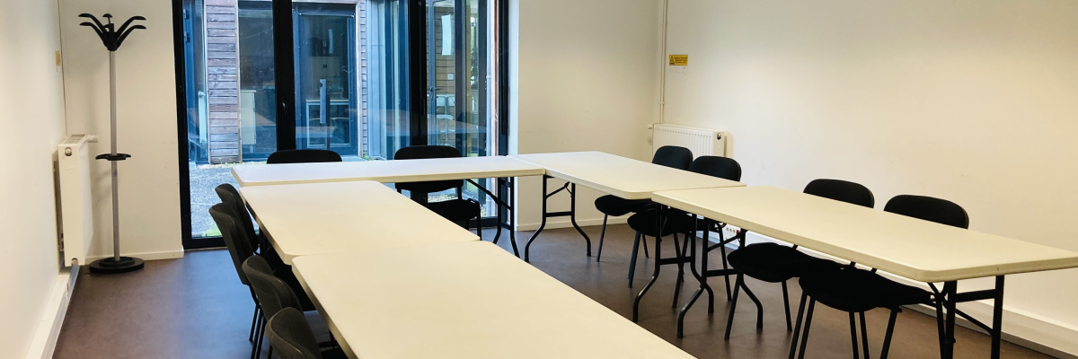 Salle avec tables, chaises, porte-manteau, radiateurs et fenêtres.