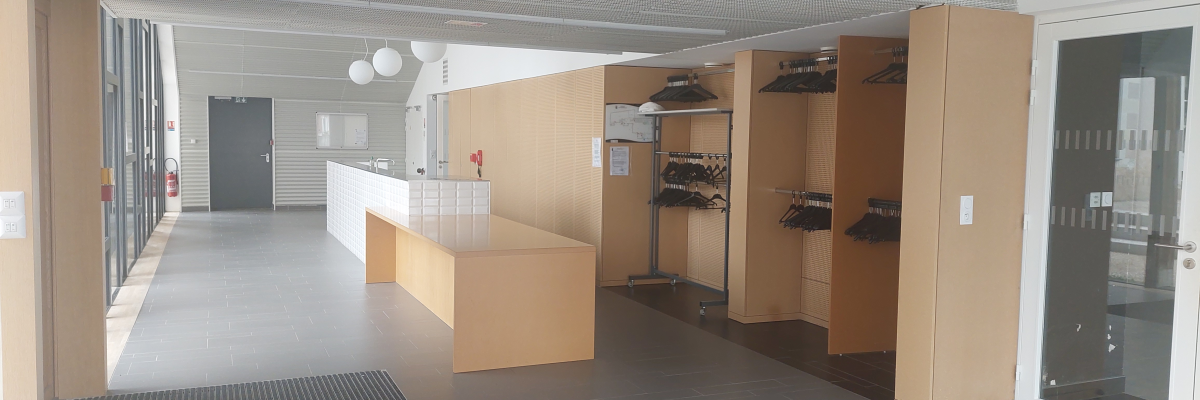 Hall d'accueil avec bureau, portemanteaux, lampes et portes vitrées.