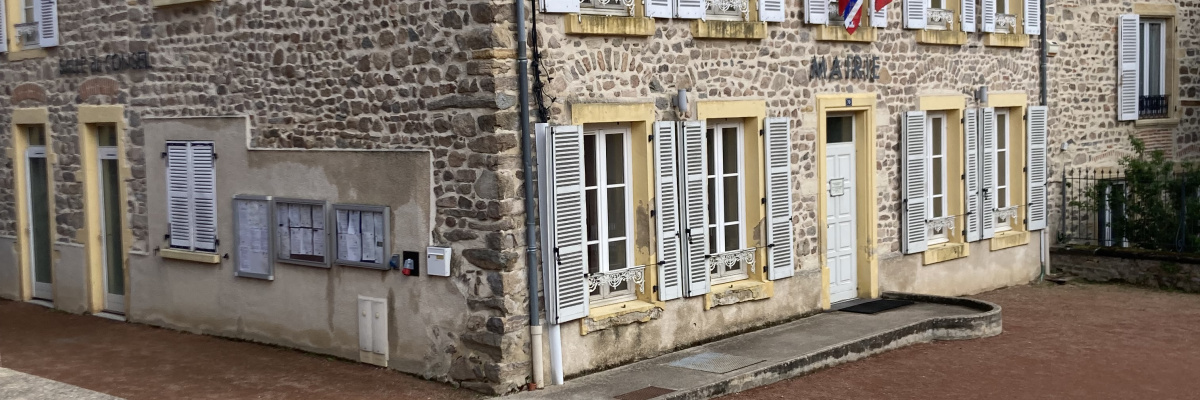 Bâtiment en pierre avec fenêtres, portes, drapeaux, et boîtes aux lettres. Rue pavée.