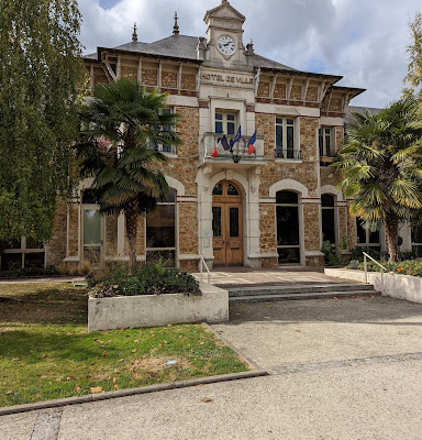"Bâtiment municipal avec horloge, drapeaux et marches."