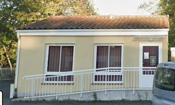 Maison avec toit en tuiles, murs beiges, trois fenêtres avec rideaux bruns, porte d'entrée, rampe blanche et voiture garée.