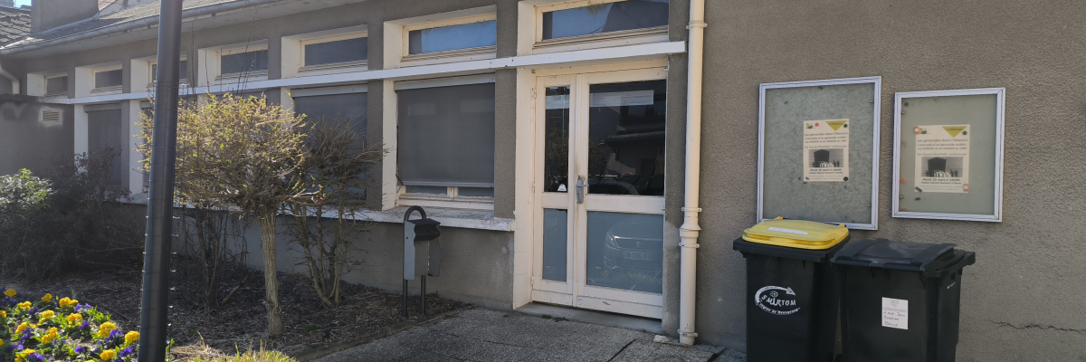 Bâtiment avec porte, fenêtres, deux poubelles et fleurs devant.