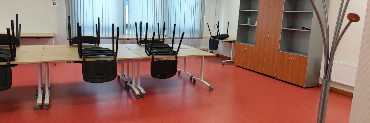 Salle avec tables, chaises, armoire et porte-manteaux.