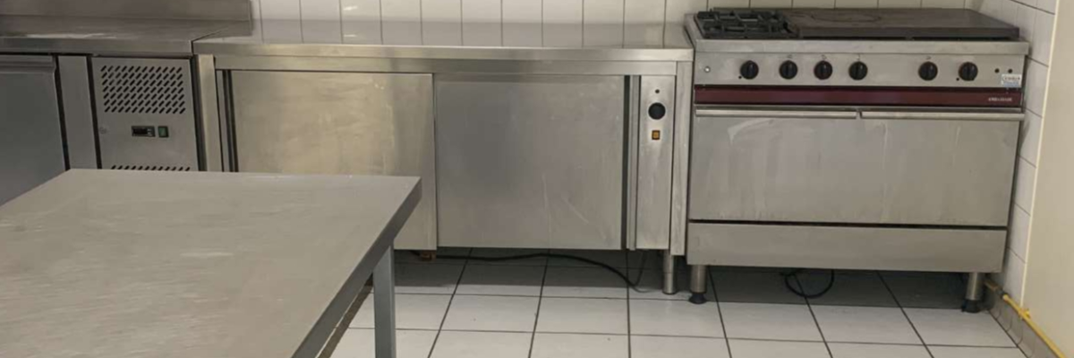 Cuisine avec plans de travail, four, plaque de cuisson, hotte et carrelage mural.