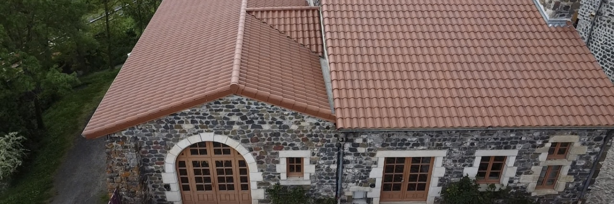 Maison en pierre avec toit en tuiles, portes et fenêtres en bois, et allée en gravier.