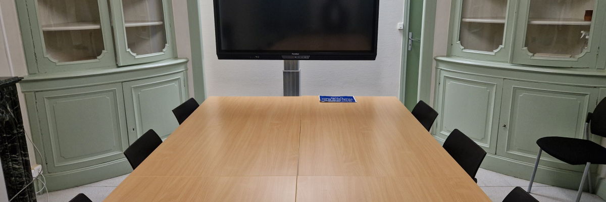 Salle de réunion avec table, chaises, écran et armoires.