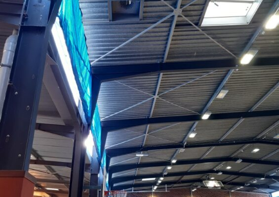 Gymnase avec filets, panneaux de score, gradins, éclairage et toit métallique.