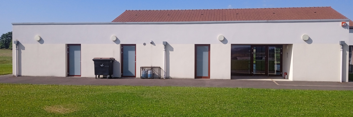 Bâtiment blanc avec toiture rouge, portes et fenêtres, poubelle et table à l'extérieur.