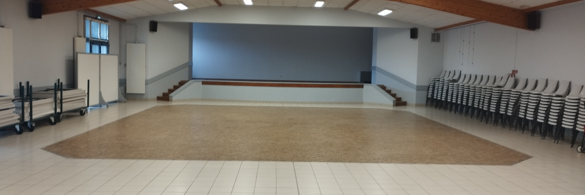 Salle avec plancher en bois, chaises alignées, rampes et portes au fond.