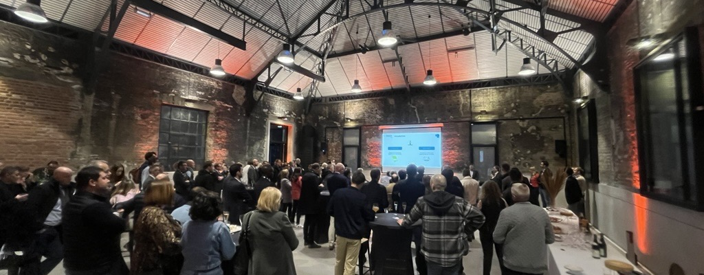 Salle avec écluses industrielles, lumières suspendues, projecteur d'images, tables, chaises et public.
