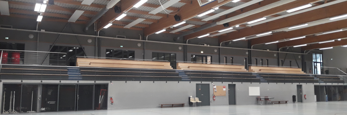 Salle de sport avec panier de basket, gradins et éclairage.