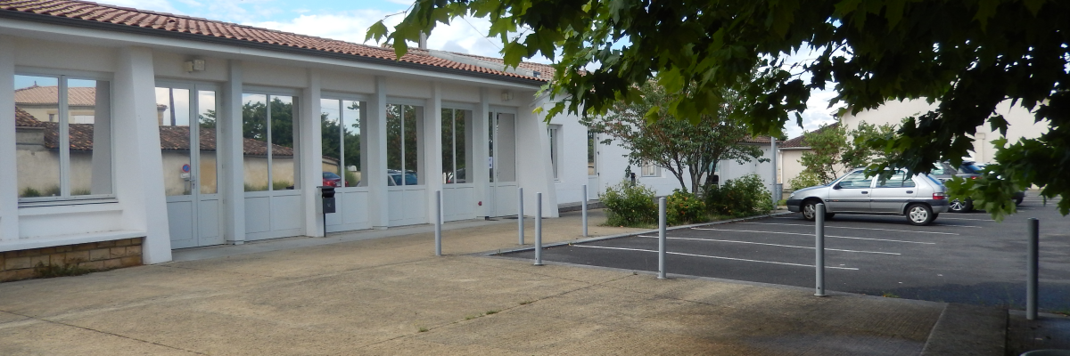 Bâtiment avec grandes fenêtres, parking et arbre.