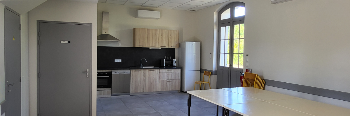 Cuisine avec table, chaises, frigo, four, meubles, placard, hottes et climatiseurs.