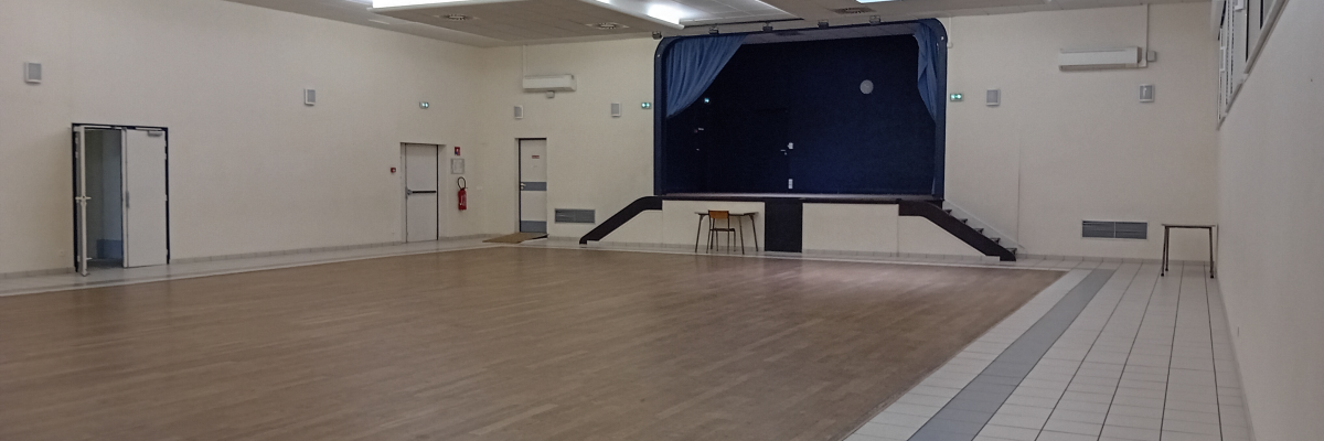 Salle vide avec parquet, estrade, écran, tabouret, portes et climatiseurs.