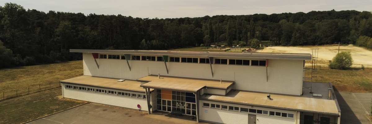 Bâtiment avec parking, forêt en arrière-plan.
