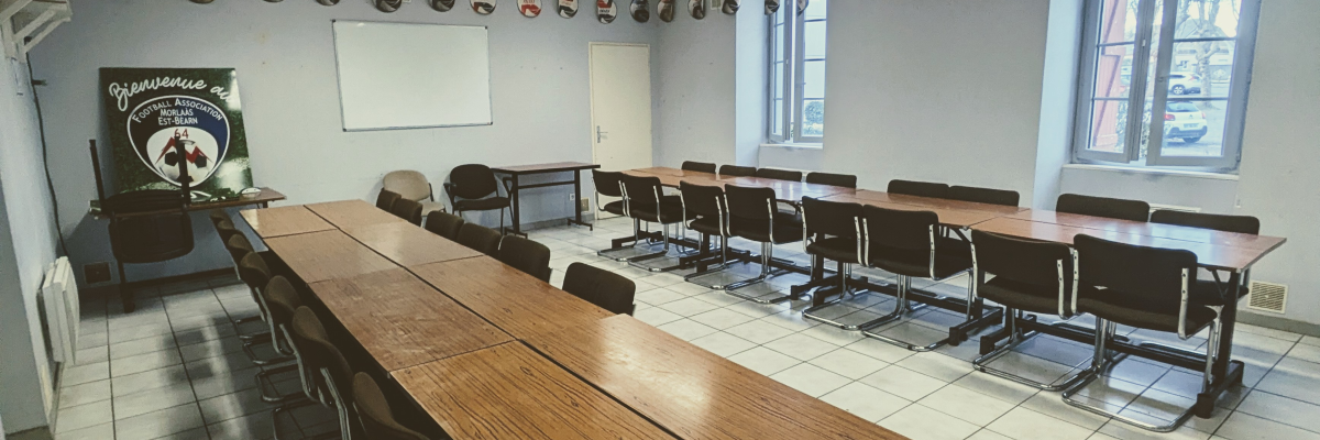Salle de classe avec tableau, table, chaises, armoire, et fenêtres.