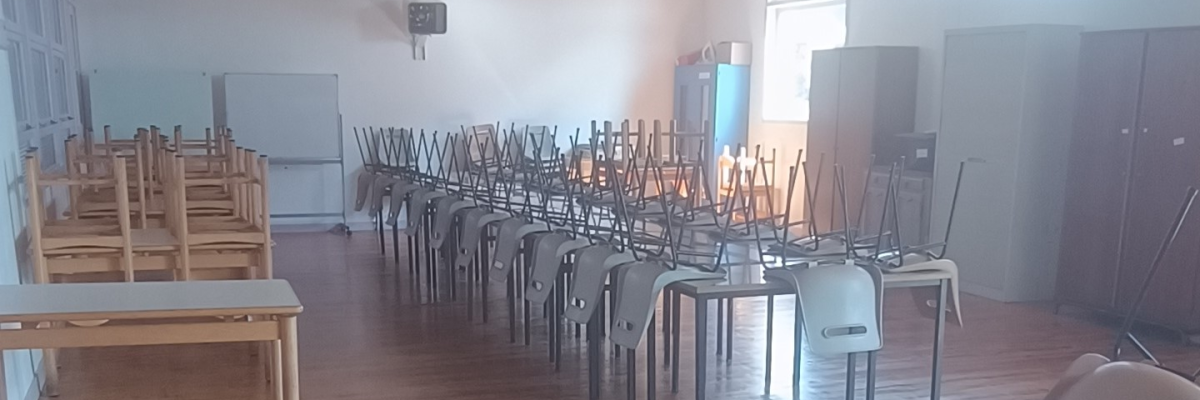 "Salle de classe avec rangées de tables, chaises, tableau blanc et climatiseur mural."