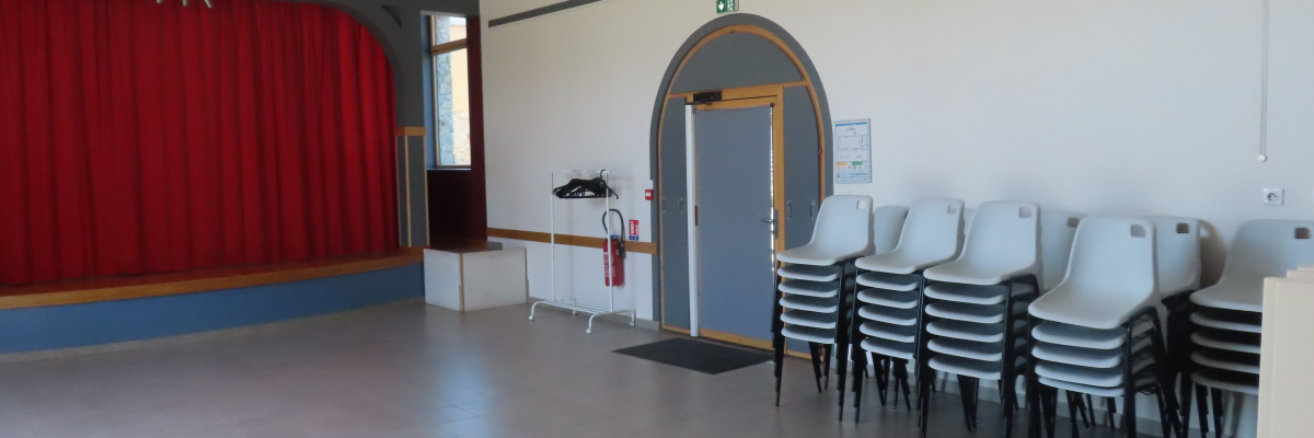 Salle avec rideau rouge, porte, chaises empilées et extincteur.