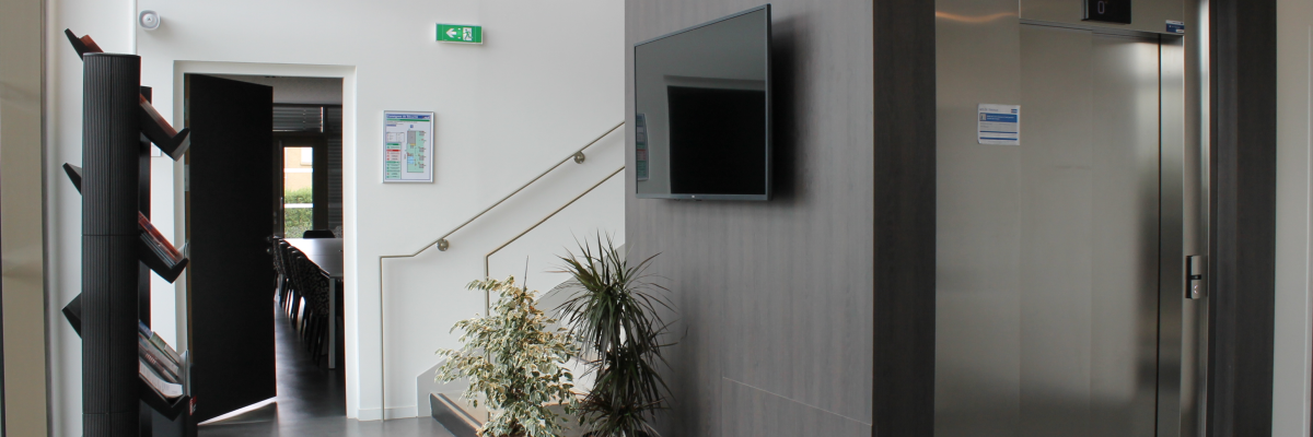 Hall d'entrée avec ascenseur, écran mural, plantes, porte et porte-manteau.