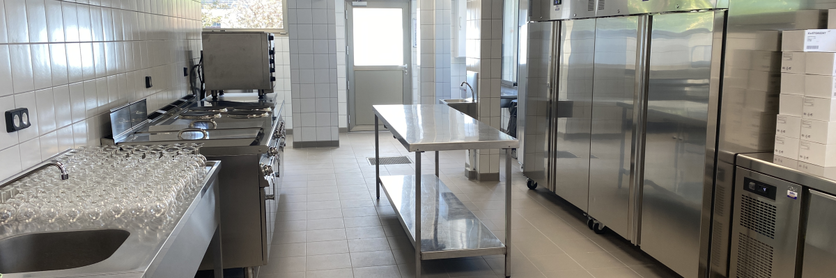 Cuisine avec plans de travail, éviers, fours, réfrigérateurs, tables inox, hottes et carrelage.