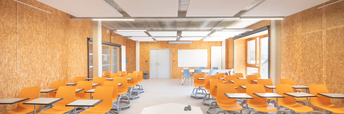 Salle de classe avec table, chaises, tableau blanc et lumières suspendues.