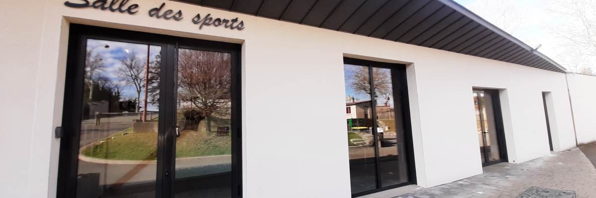 Salle des sports avec portes vitrées, pots de fleurs et murs en gabion.