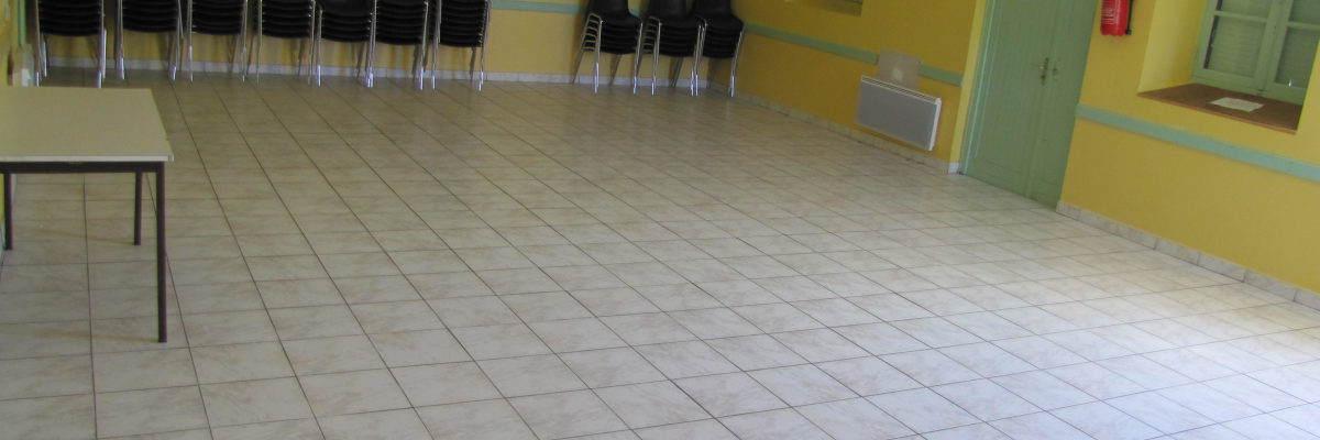 Salle avec chaises alignées, table, porte verte, extincteur et radiateur.