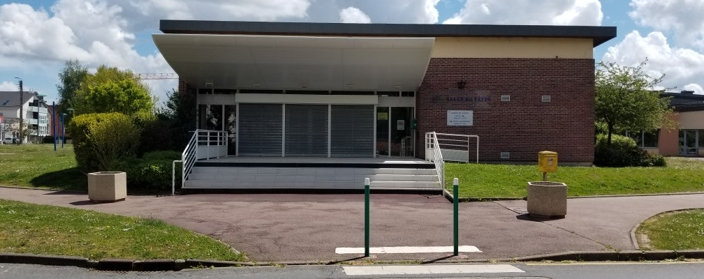 Bâtiment avec devantée en béton, rampes d'accès, passage piéton et paniers à déchets.