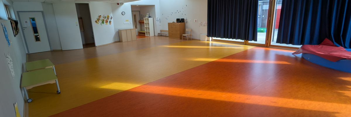 Salle spacieuse avec sol coloré, chaises, tables d'activité et rideaux.