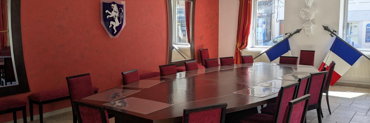 Salle avec table, chaises, lustres, drapeaux et armoire.