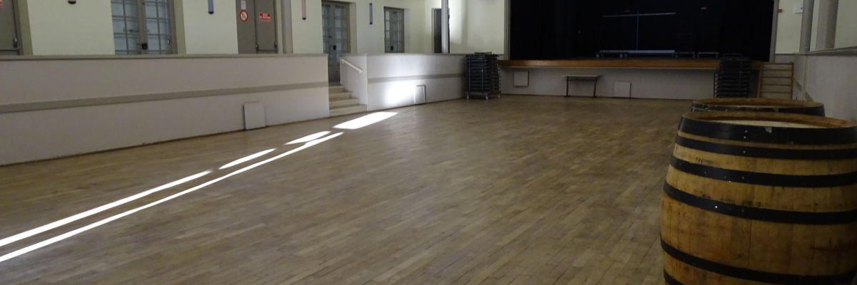 Grande salle avec parquet, tonneau, barreaux, échafaudage, murs blancs et portes rouges.