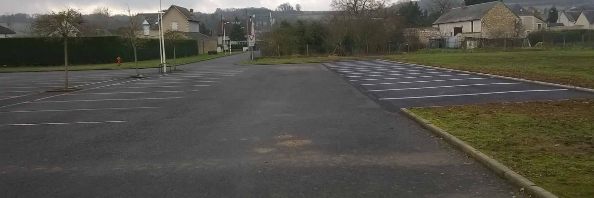 Parking vide avec bornes, lampadaires et maisons en arrière-plan.