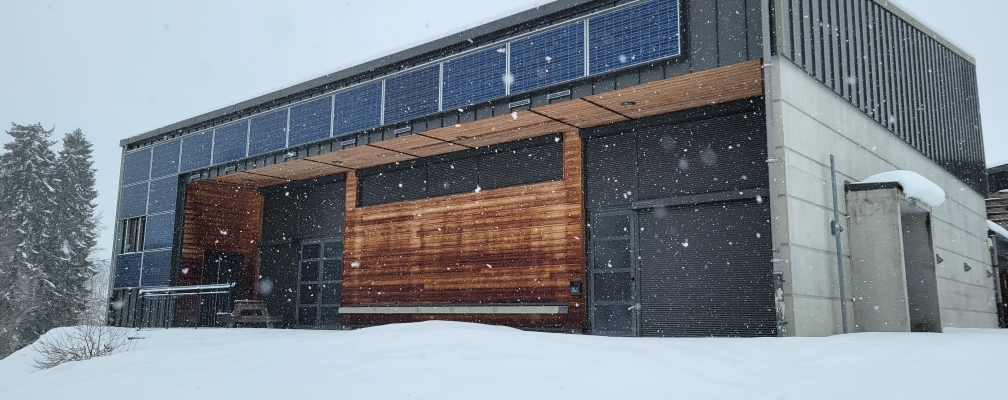 Bâtiment moderne avec panneaux solaires, portes en bois et neige.
