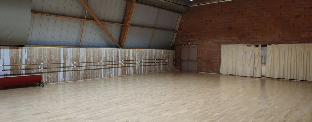 Salle de danse avec parquet, barre, miroir, rideau et matelas rouge.