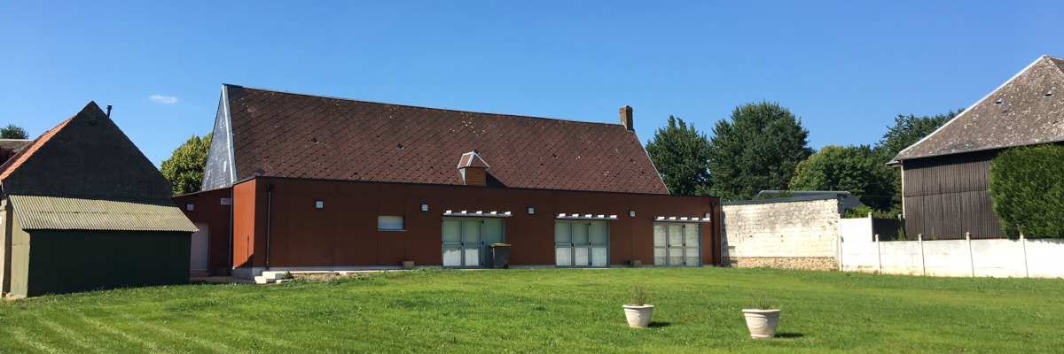 Maison avec toit rouge, trois vasques sur pelouse, ciel bleu.