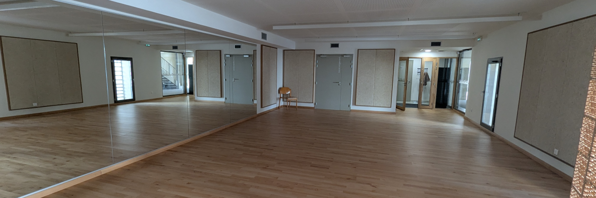 Salle vide avec parquet, miroirs, portes et plafonds suspendus.