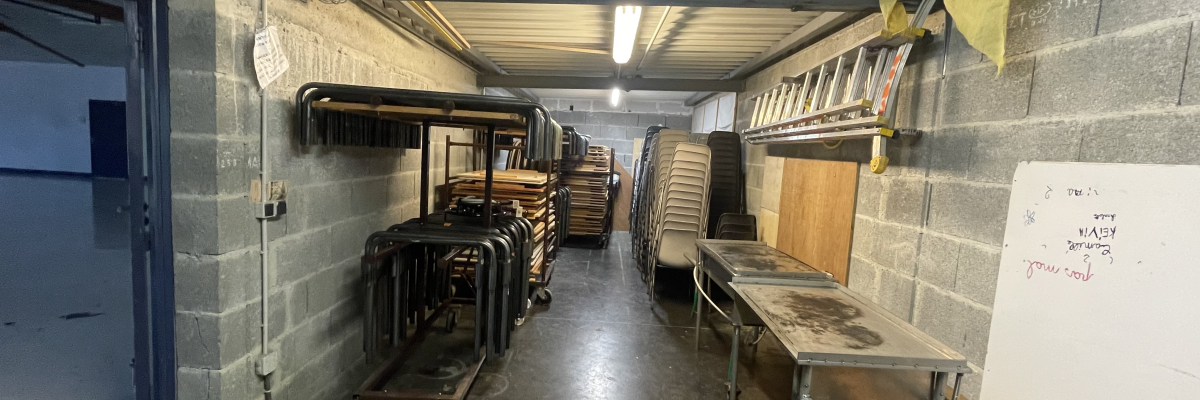 Atelier avec étagères, chariots, tables, échelles, outils et panneaux d'affichage.
