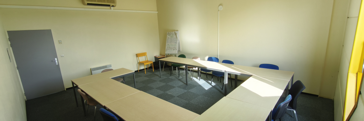 Salle de réunion avec tables, chaises, climatiseur et tableau blanc.